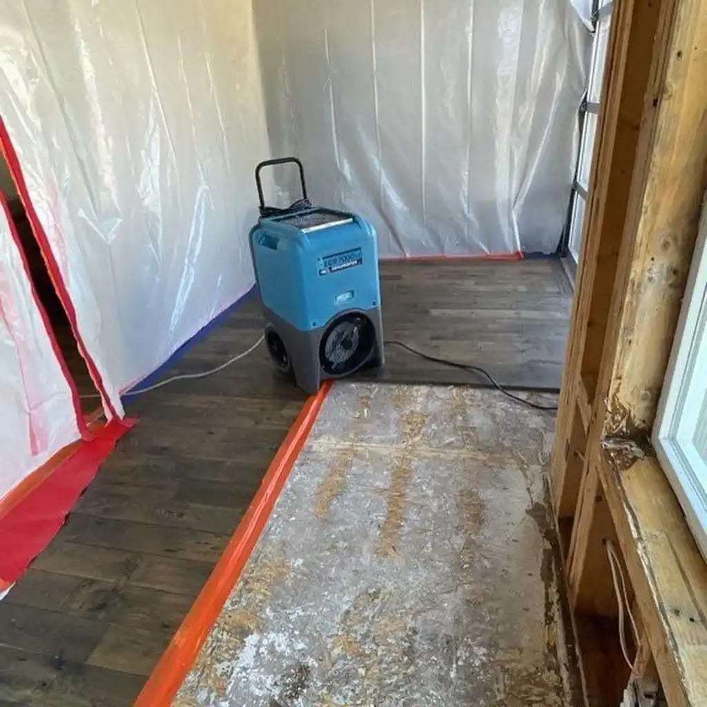 Dehumidifier running inside a plastic containment with the flooring removed